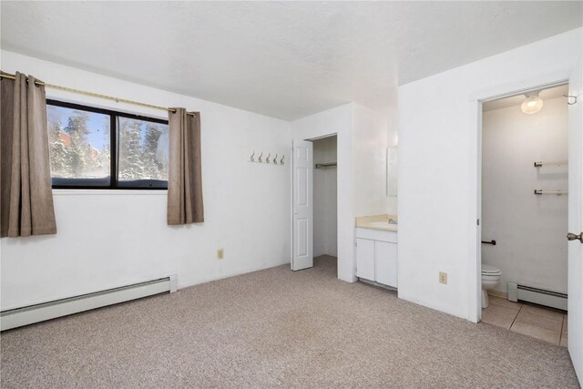 unfurnished bedroom with light carpet, baseboard heating, and ensuite bathroom