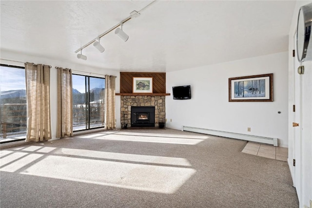 unfurnished living room with a fireplace, rail lighting, baseboard heating, carpet flooring, and a mountain view