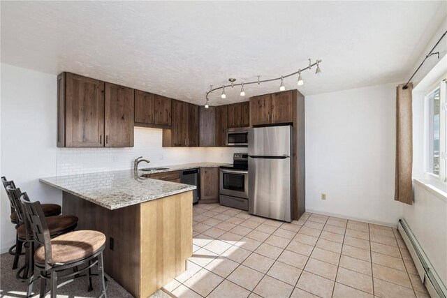 kitchen with tasteful backsplash, a peninsula, baseboard heating, stainless steel appliances, and a sink