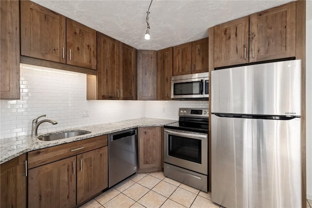 kitchen featuring light tile patterned floors, stainless steel appliances, backsplash, a sink, and a textured ceiling