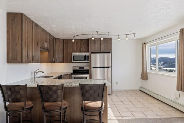 kitchen with stainless steel appliances, a baseboard radiator, tasteful backsplash, a sink, and a peninsula