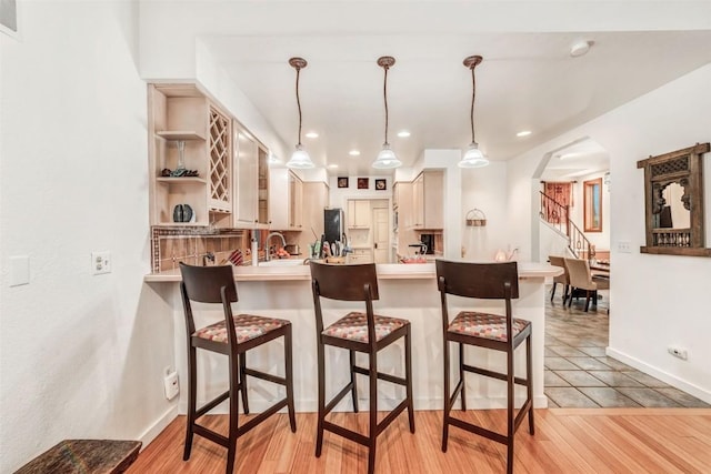 kitchen featuring light brown cabinetry, light tile patterned floors, decorative light fixtures, and a breakfast bar