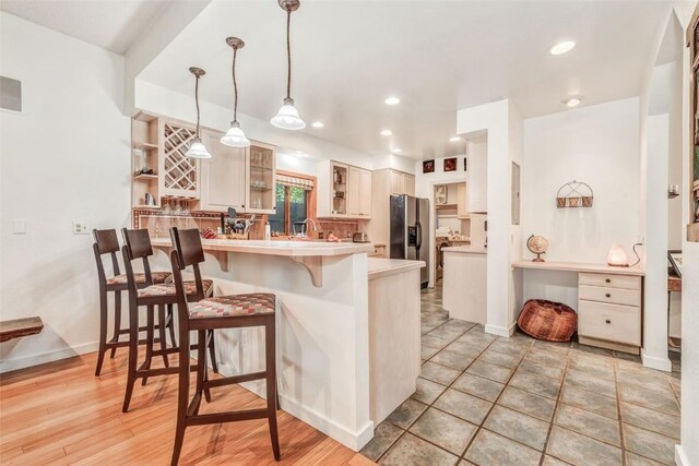 kitchen with sink, a breakfast bar, stainless steel refrigerator with ice dispenser, decorative light fixtures, and kitchen peninsula