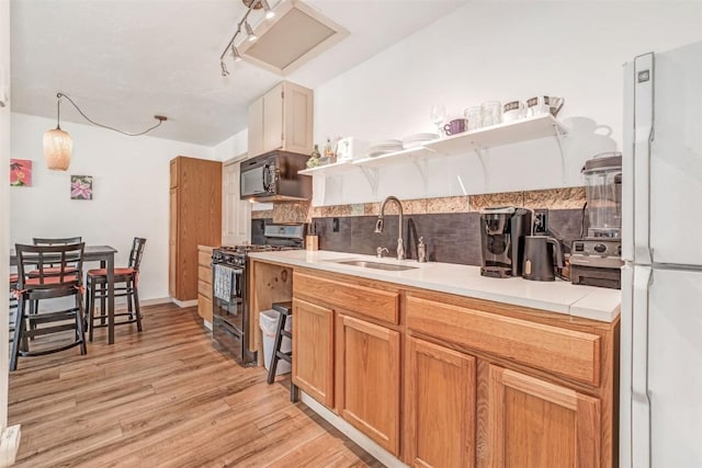 kitchen featuring pendant lighting, sink, black appliances, light hardwood / wood-style floors, and decorative backsplash