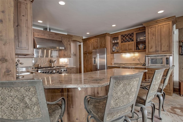 kitchen with sink, stainless steel appliances, a kitchen breakfast bar, range hood, and kitchen peninsula