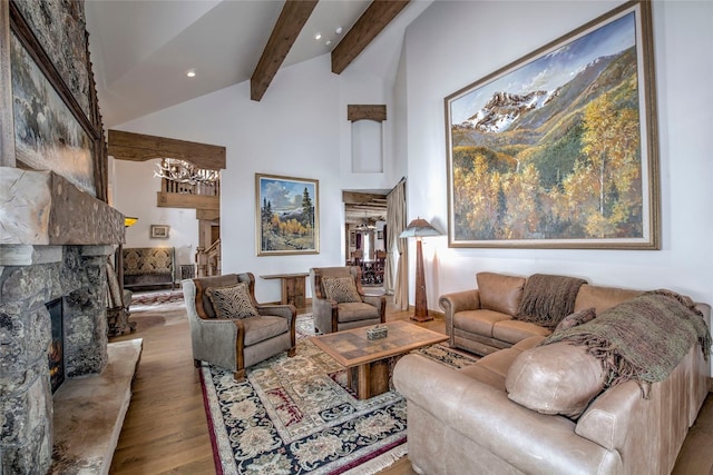 living room with lofted ceiling with beams, light hardwood / wood-style flooring, a stone fireplace, and a notable chandelier