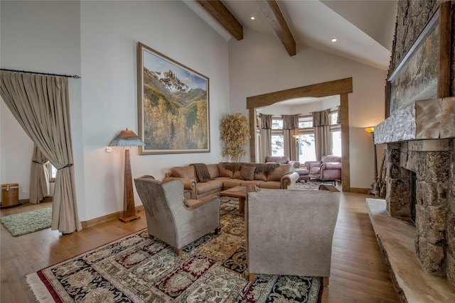 living room featuring light hardwood / wood-style floors, a stone fireplace, a towering ceiling, and beam ceiling