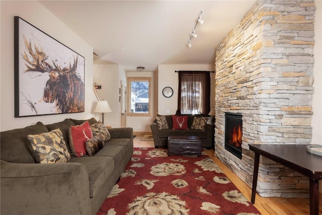 living room featuring hardwood / wood-style flooring, rail lighting, and a stone fireplace