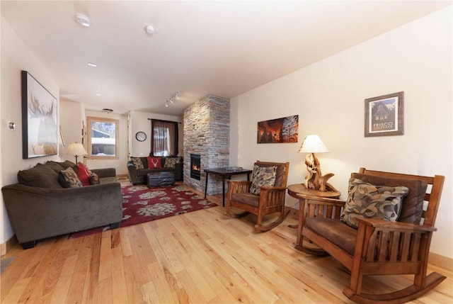 living room with a stone fireplace, track lighting, and light hardwood / wood-style floors