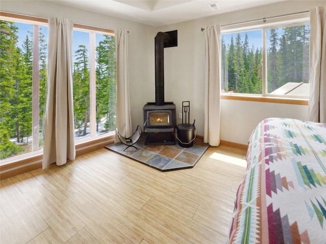 bedroom with light wood-type flooring, a wood stove, and multiple windows