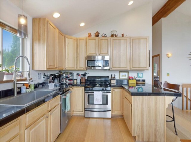 kitchen featuring a breakfast bar, sink, light brown cabinetry, decorative light fixtures, and stainless steel appliances