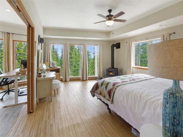 bedroom with light wood-type flooring, a wood stove, and ceiling fan