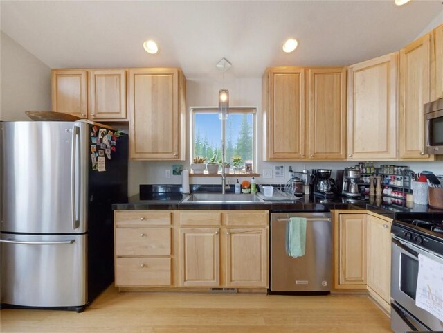 kitchen with appliances with stainless steel finishes, light brown cabinetry, sink, light hardwood / wood-style flooring, and hanging light fixtures