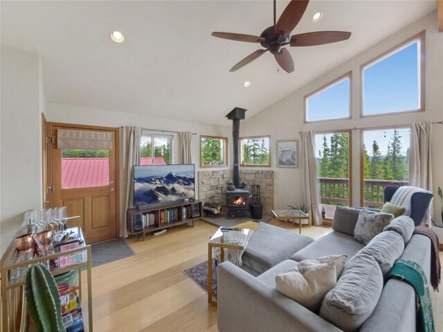 living room with ceiling fan, light hardwood / wood-style floors, a wood stove, and high vaulted ceiling