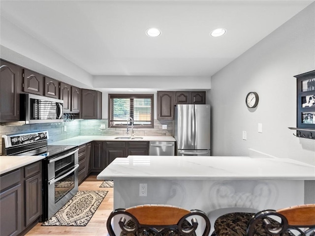 kitchen featuring appliances with stainless steel finishes, tasteful backsplash, dark brown cabinetry, sink, and light hardwood / wood-style flooring