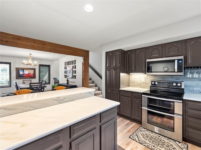 kitchen featuring decorative backsplash, appliances with stainless steel finishes, light wood-type flooring, beamed ceiling, and a chandelier