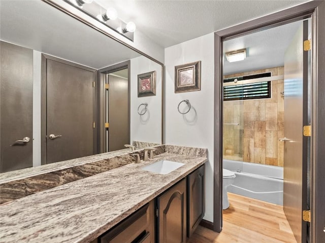 full bathroom with vanity, tiled shower / bath, toilet, a textured ceiling, and wood-type flooring