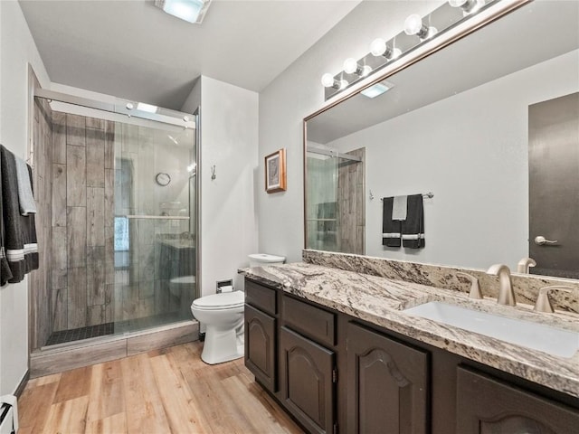 bathroom featuring hardwood / wood-style floors, vanity, toilet, baseboard heating, and a shower with shower door