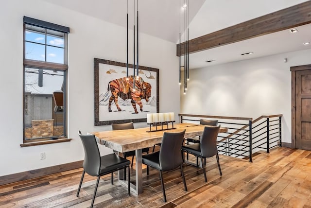 dining room with hardwood / wood-style flooring and vaulted ceiling with beams