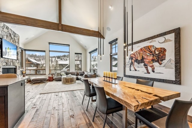 dining space with a fireplace, beamed ceiling, high vaulted ceiling, and hardwood / wood-style flooring