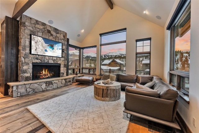 living room featuring hardwood / wood-style flooring, beam ceiling, a stone fireplace, and high vaulted ceiling