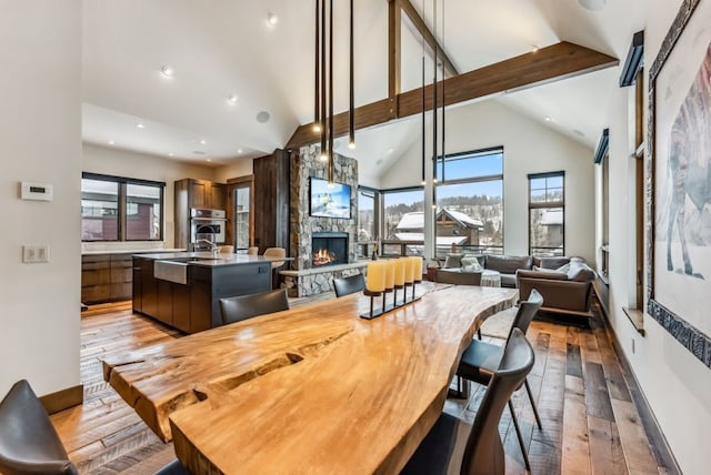 dining space featuring plenty of natural light, a stone fireplace, light wood-type flooring, and high vaulted ceiling