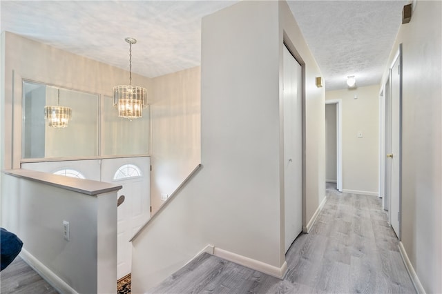 hallway with a chandelier, light hardwood / wood-style flooring, and a textured ceiling