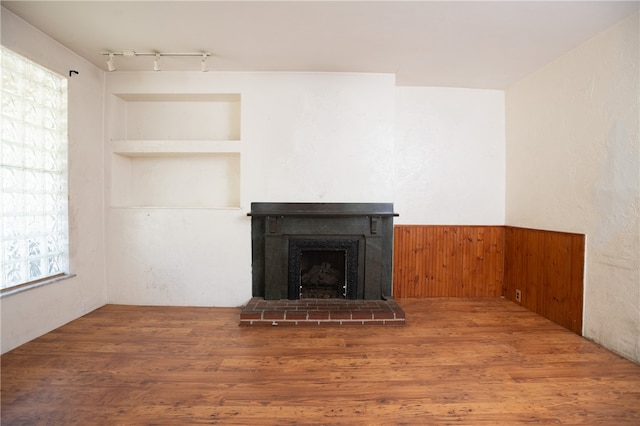 unfurnished living room with plenty of natural light, a brick fireplace, rail lighting, and built in features