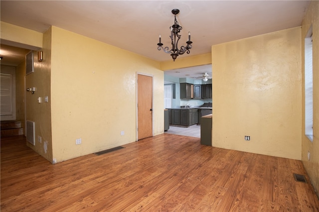 empty room featuring ceiling fan with notable chandelier and light wood-type flooring