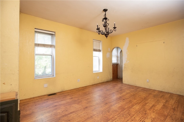 spare room featuring an inviting chandelier, a wealth of natural light, and wood-type flooring