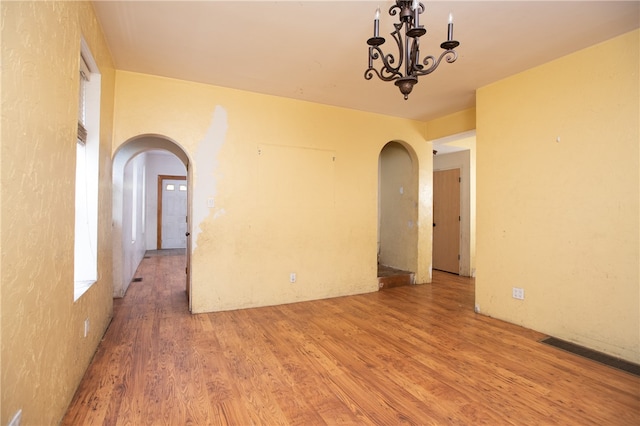 unfurnished room featuring an inviting chandelier and light wood-type flooring