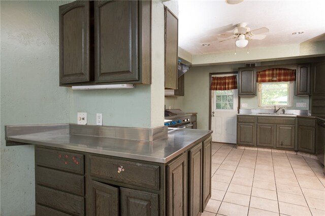 kitchen featuring dark brown cabinetry, stainless steel counters, ceiling fan, sink, and light tile flooring