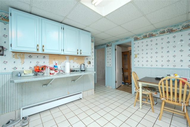 kitchen with a baseboard radiator, white cabinetry, a paneled ceiling, and light tile floors