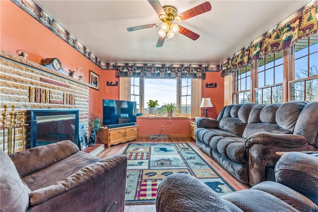 living room with wood-type flooring, a brick fireplace, and ceiling fan