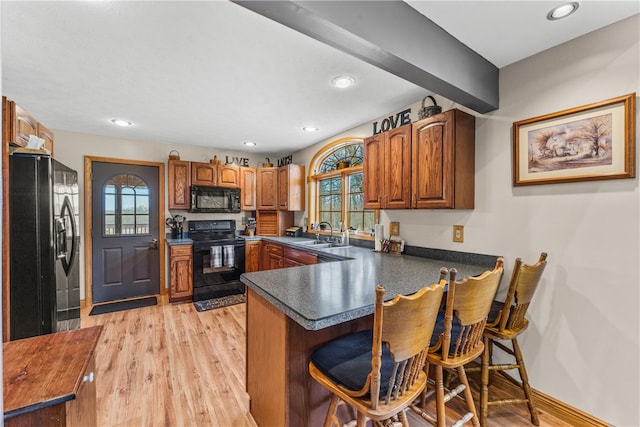 kitchen with light wood-type flooring, black appliances, kitchen peninsula, sink, and a breakfast bar area