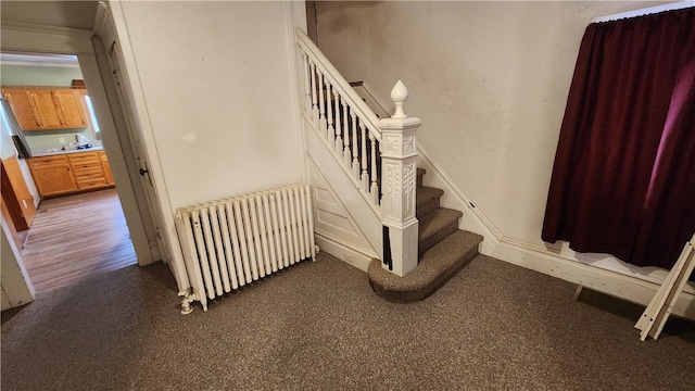 stairs with dark colored carpet and radiator