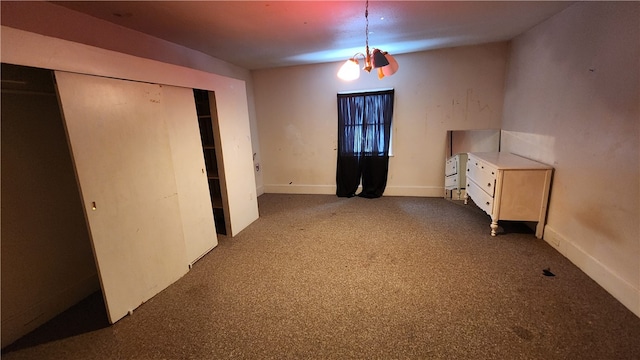 unfurnished bedroom with dark colored carpet, an inviting chandelier, and a closet