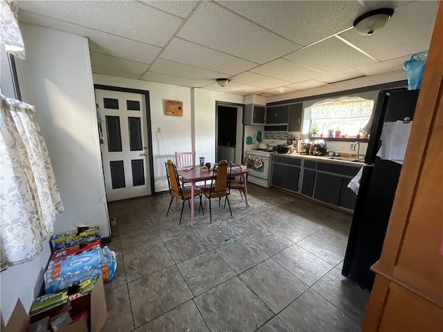 kitchen featuring black fridge, dark tile patterned flooring, sink, a drop ceiling, and white gas stove