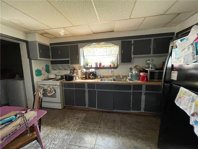 kitchen with dark tile patterned flooring, sink, a drop ceiling, white gas range, and black refrigerator