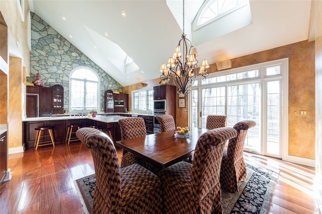 dining room featuring a skylight, hardwood / wood-style floors, a notable chandelier, and high vaulted ceiling