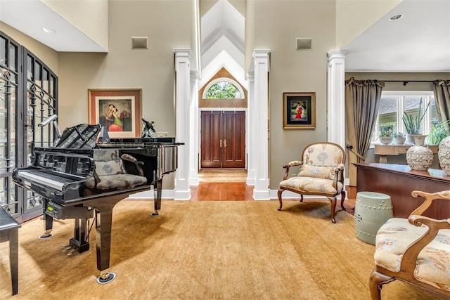 living area with a towering ceiling, light hardwood / wood-style floors, and ornate columns