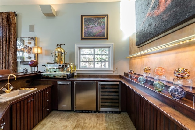 bar with wine cooler, light hardwood / wood-style floors, dark brown cabinets, and sink