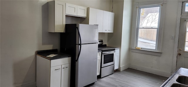 kitchen with stainless steel appliances, white cabinetry, and light hardwood / wood-style floors