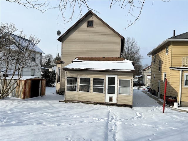 snow covered back of property featuring a storage shed