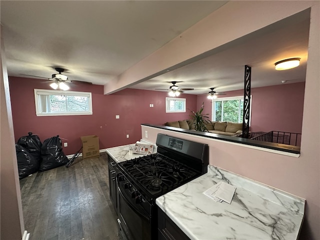 kitchen featuring ceiling fan, dark hardwood / wood-style flooring, light stone countertops, gas range, and beam ceiling