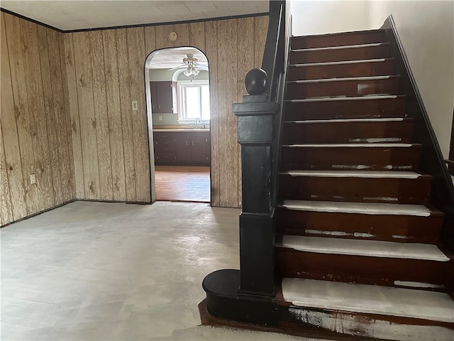 stairs with ceiling fan, wood walls, sink, and concrete flooring