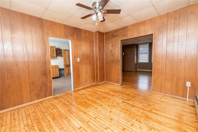 spare room with wooden walls, ceiling fan, a paneled ceiling, and light wood-type flooring