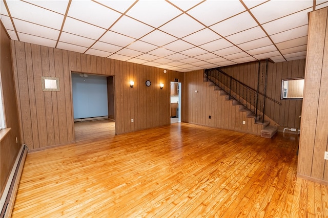 basement with a drop ceiling, light hardwood / wood-style flooring, and wooden walls