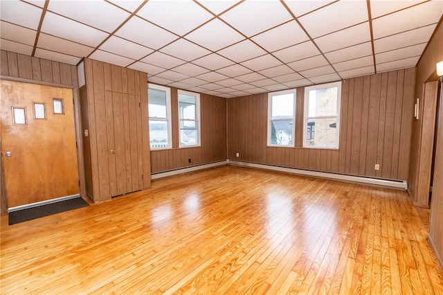 spare room with a drop ceiling, light hardwood / wood-style flooring, a healthy amount of sunlight, and baseboard heating