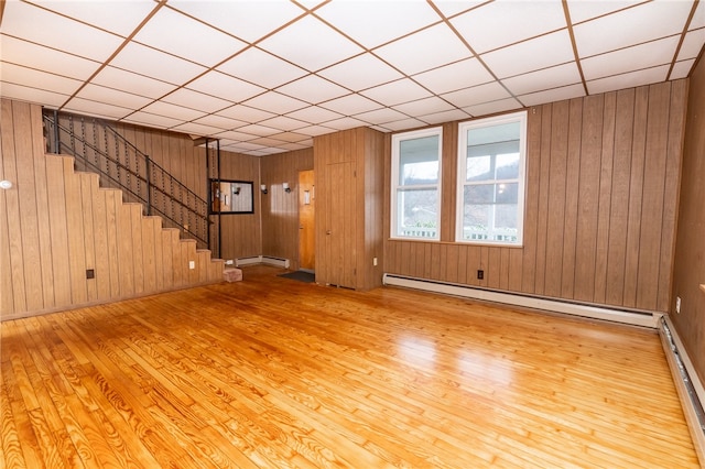 unfurnished room featuring a baseboard radiator, light hardwood / wood-style floors, a paneled ceiling, and wooden walls